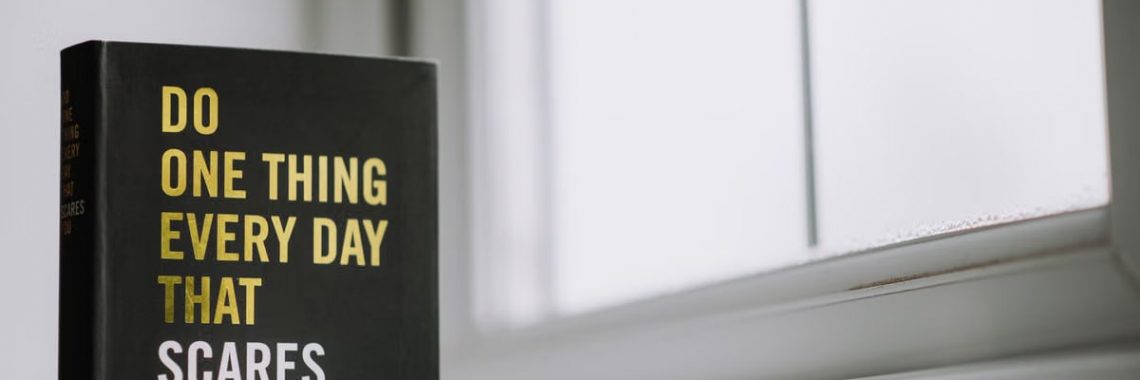 Rectangular shaped book with printed title on black hardcover on windowsill in house in daytime